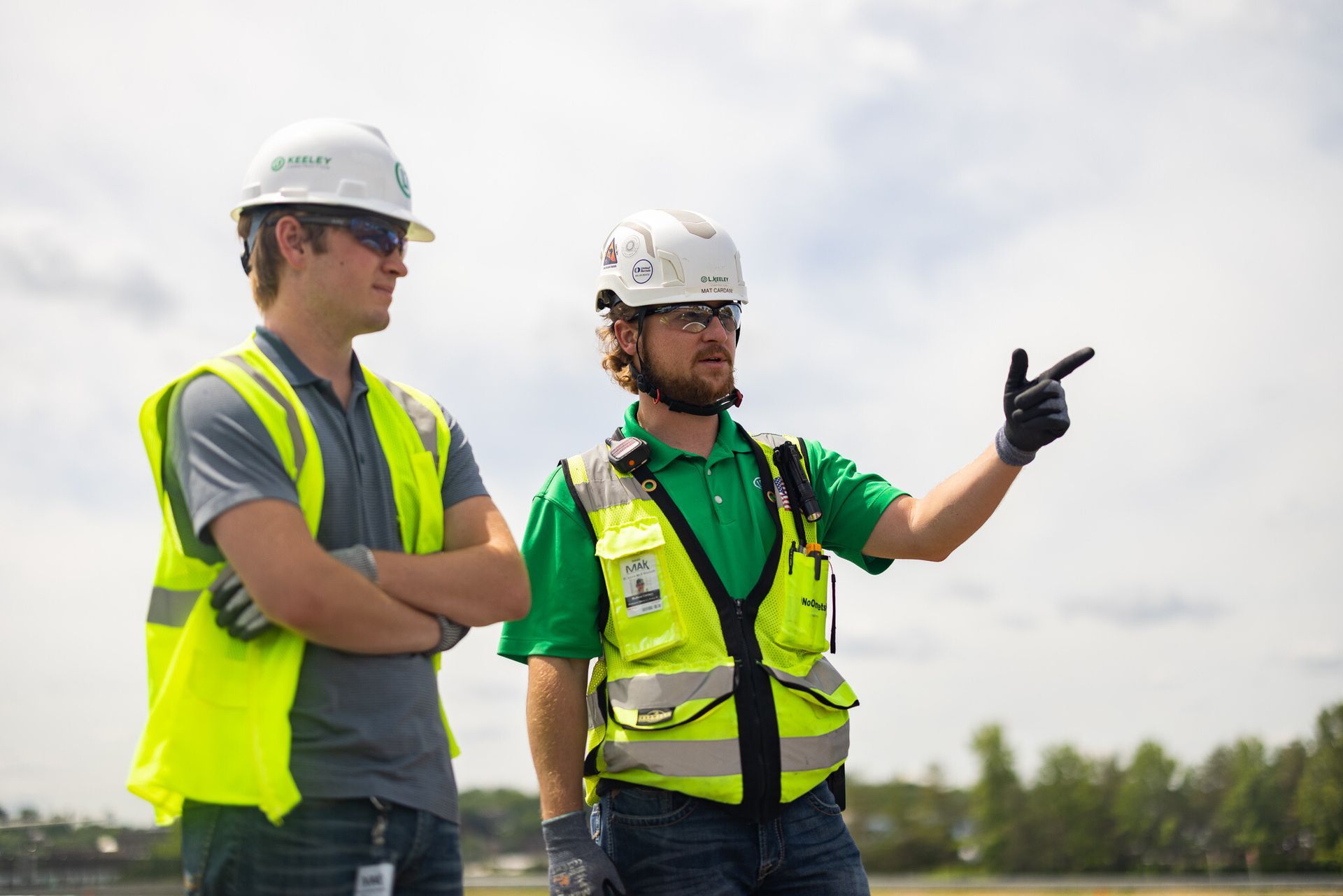 Two construction workers wearing hard hats and safety vests are standing next to each other.