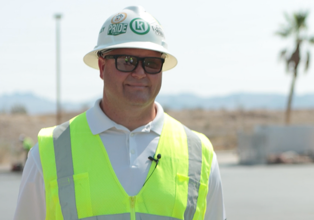 A man wearing a hard hat and safety vest is standing in front of a palm tree.