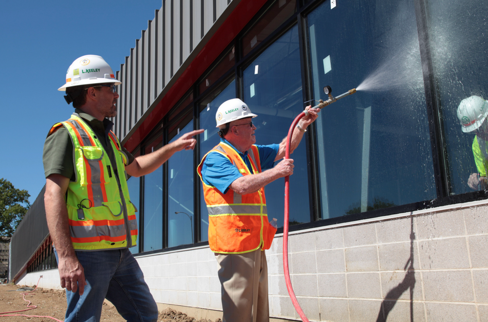 Two construction workers spraying a window with a hose