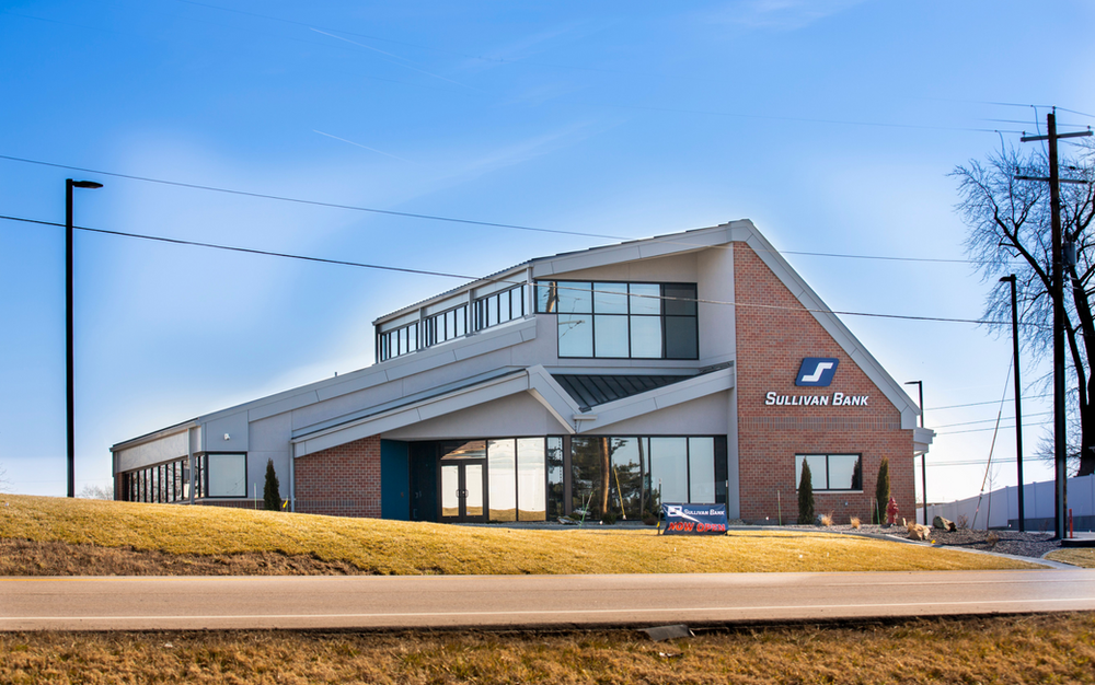 A large brick building with a lot of windows is sitting on top of a grassy hill.