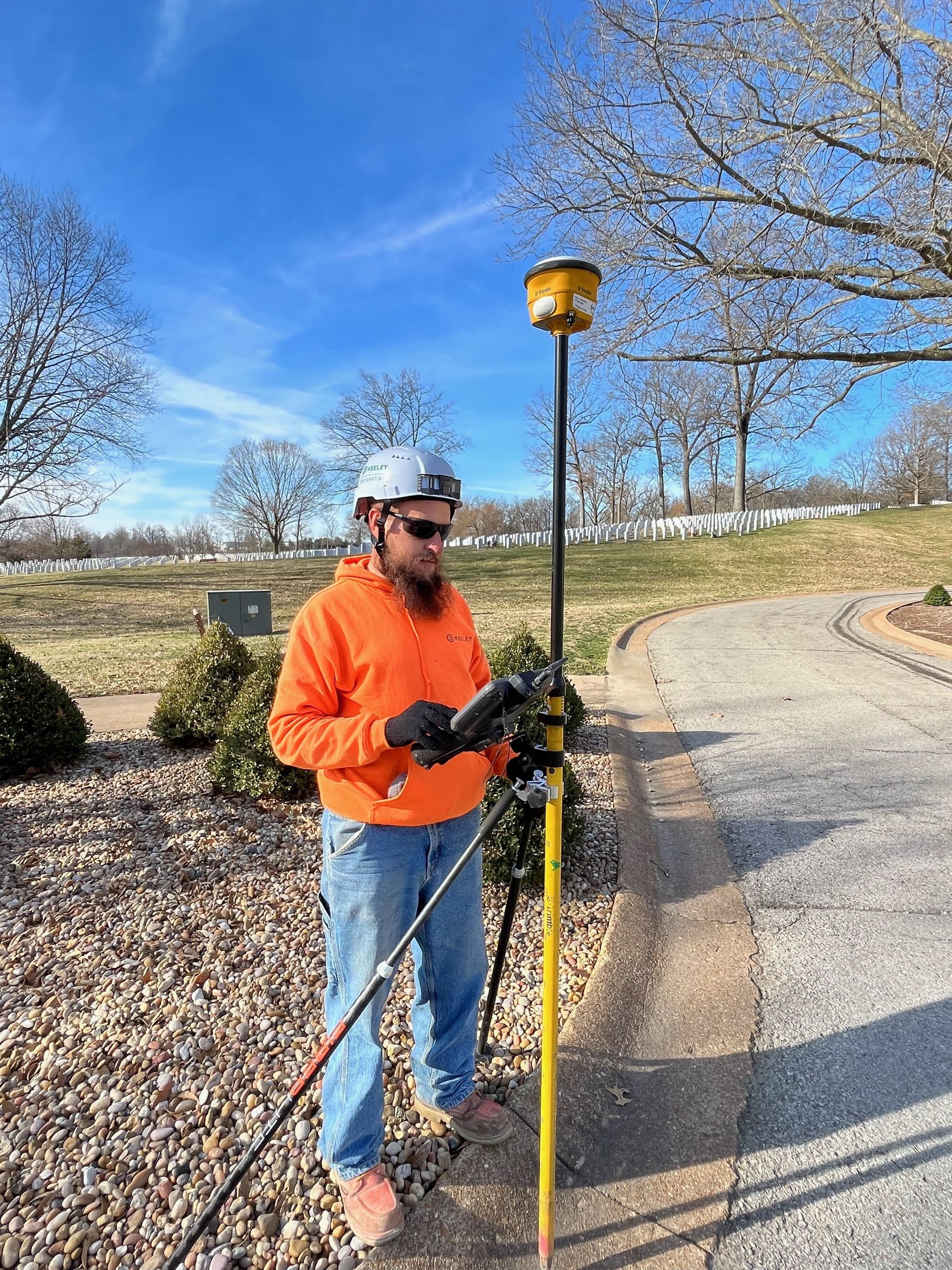 A man in an orange jacket is standing next to a pole holding a tablet.