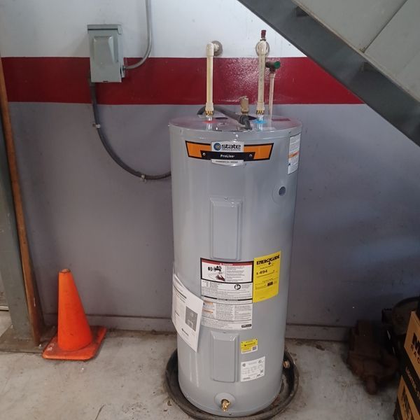 A water heater is sitting under a staircase next to an orange cone