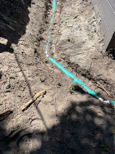 A green pipe is laying in the dirt next to a hammer.