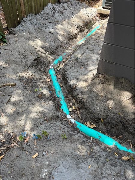 A green pipe is laying in the dirt next to a building.