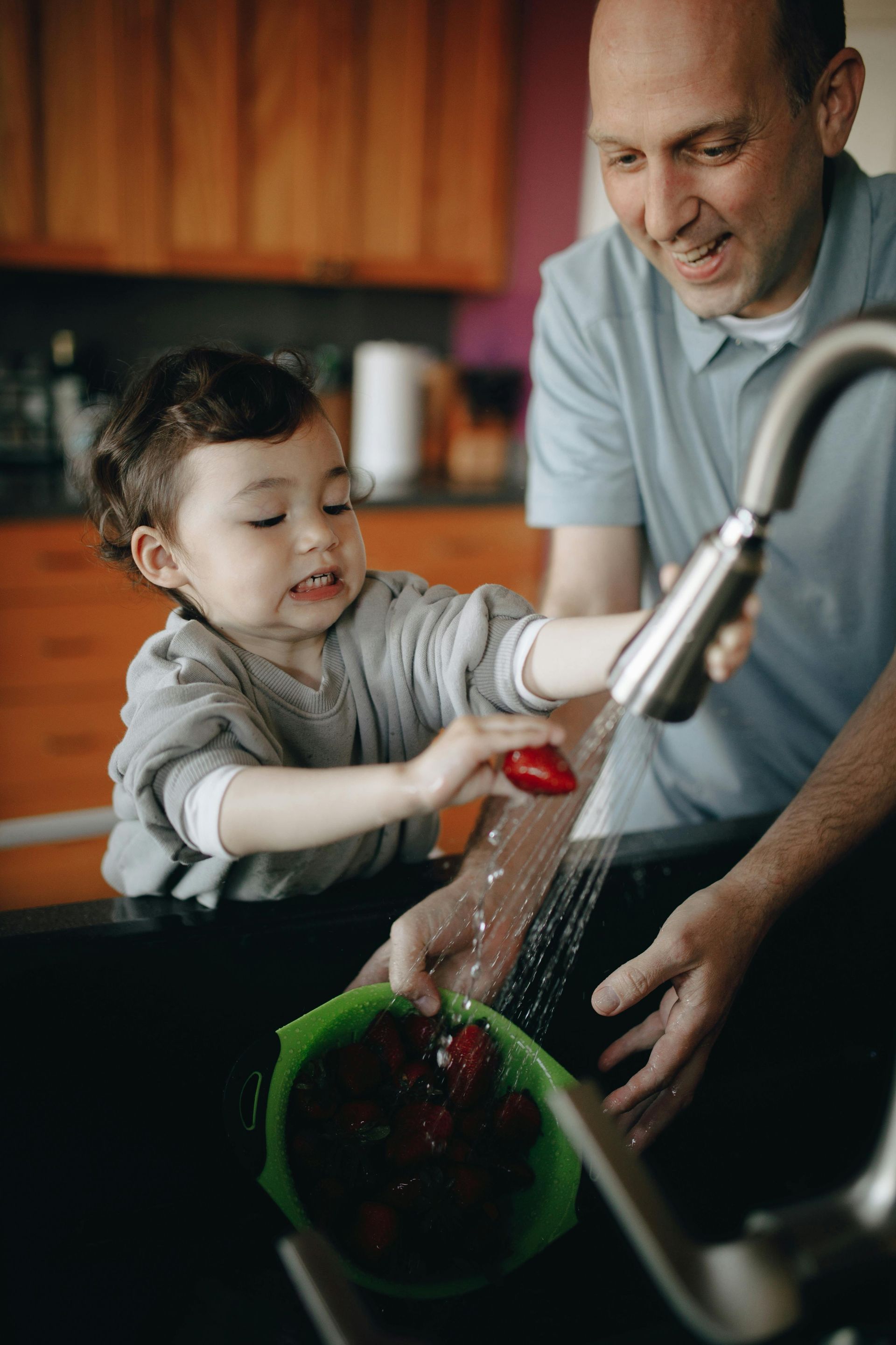 A man and a little boy are washing strawberries in a kitchen sink.