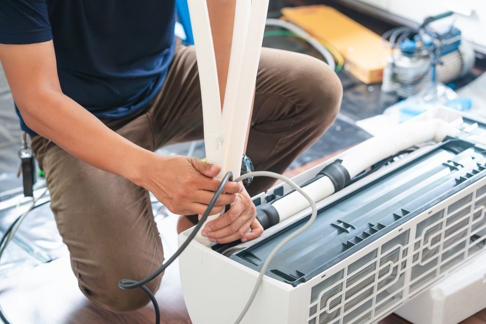 A man is kneeling down to fix an air conditioner.
