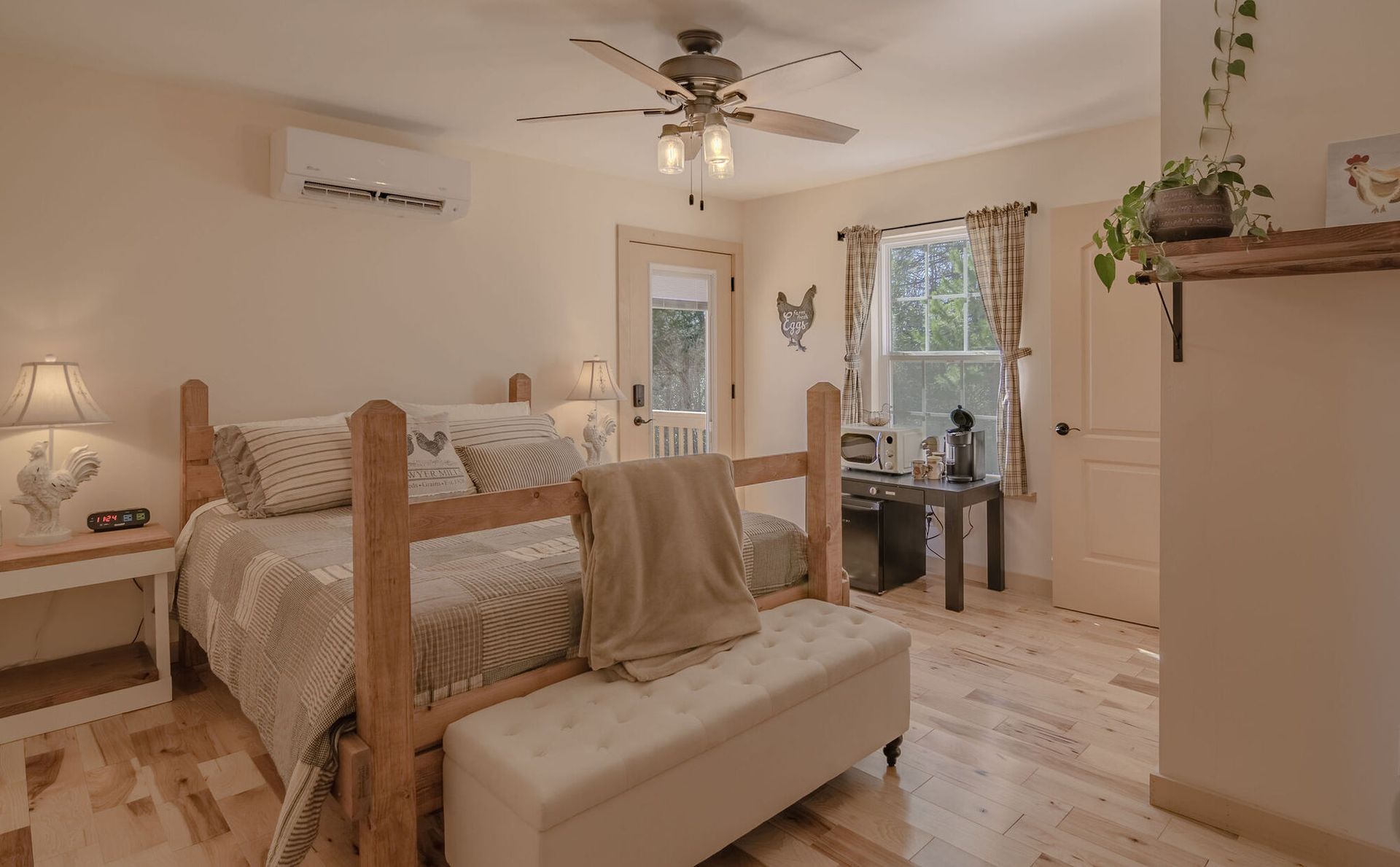 A cozy bedroom with a wooden bed, white bench, ceiling fan, desk, and light wood flooring in a bright, neutral space.