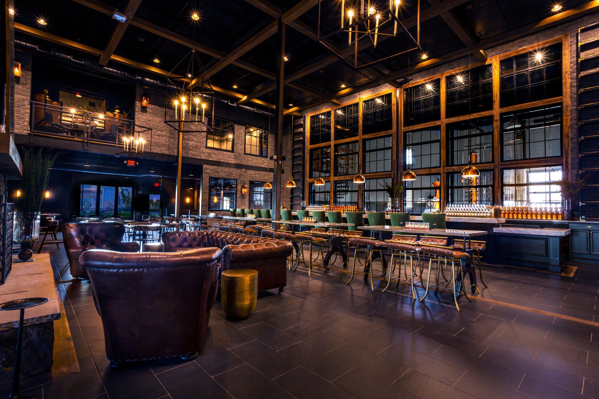 A dimly lit, upscale lounge with leather armchairs, a wooden bar, high ceilings, and warm pendant lighting.