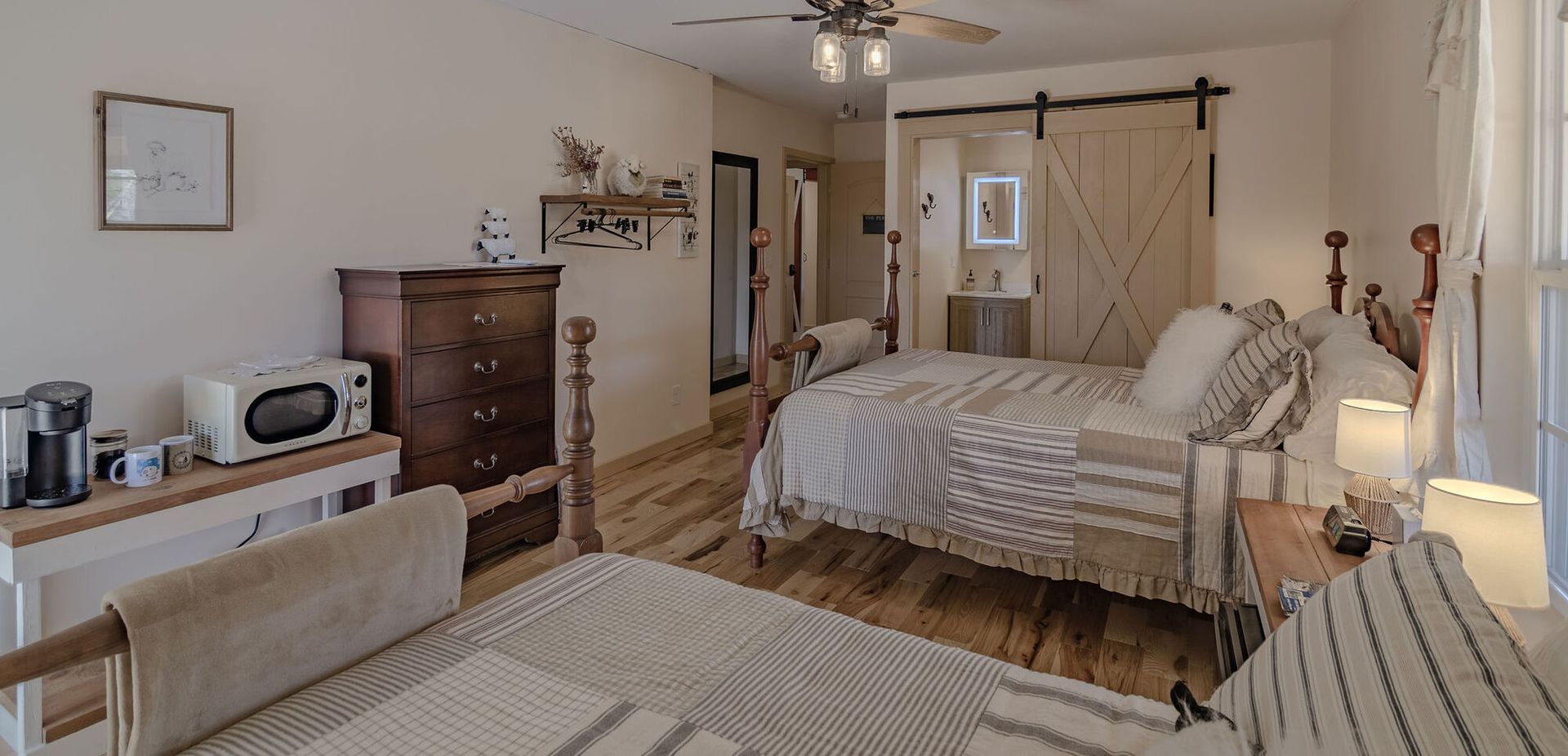 A cozy bedroom with two beds, wood floors, a dark wooden dresser, a microwave, and sliding barn doors.
