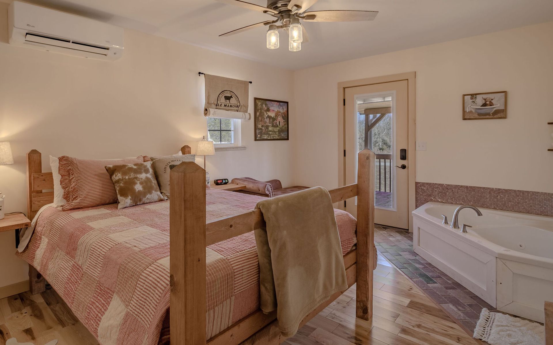 A cozy bedroom featuring a wooden bed with patterned quilts, a ceiling fan, and a built-in bathtub near a glass door.