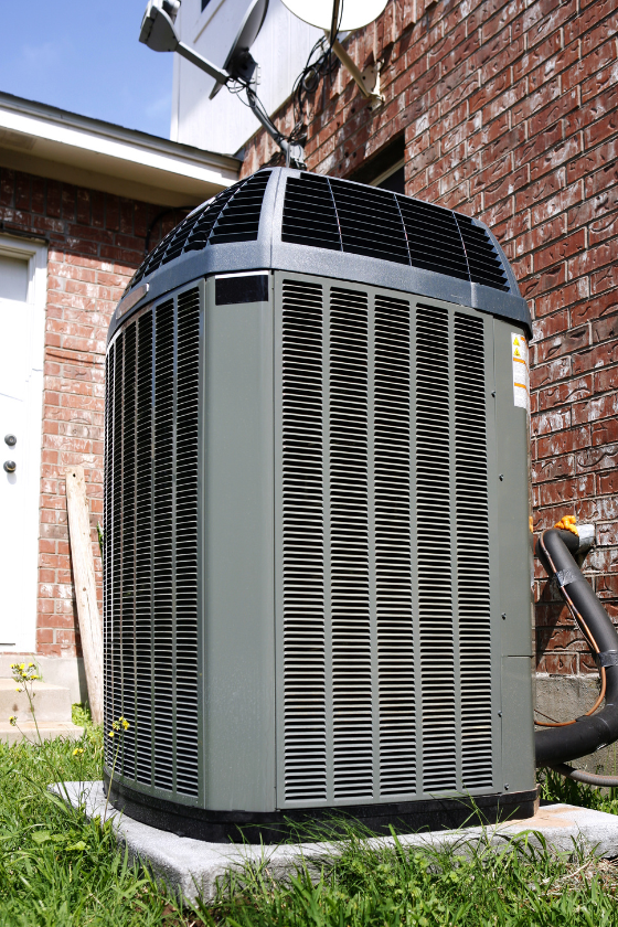 A large air conditioner is sitting in the grass in front of a brick building.