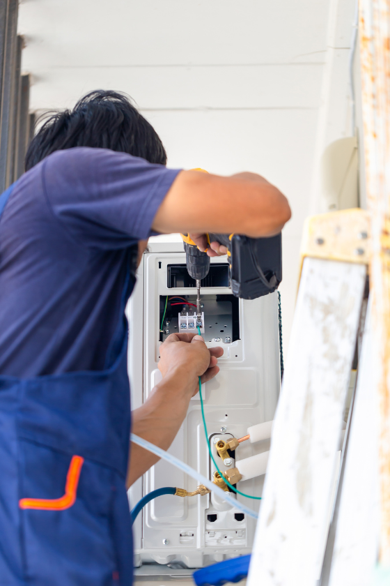 A man is using a drill to fix an air conditioner.