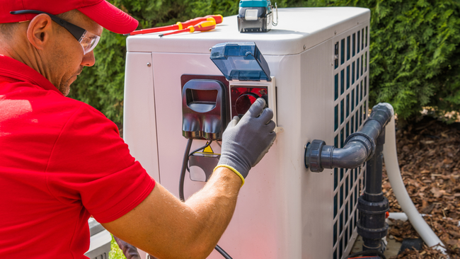 A man in a red shirt is working on a heat pump.