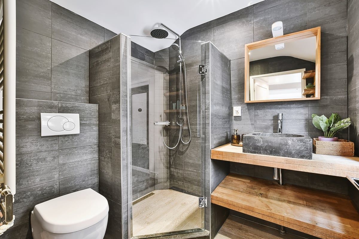 Modern gray bathroom with a glass shower, wooden vanity, and toilet.