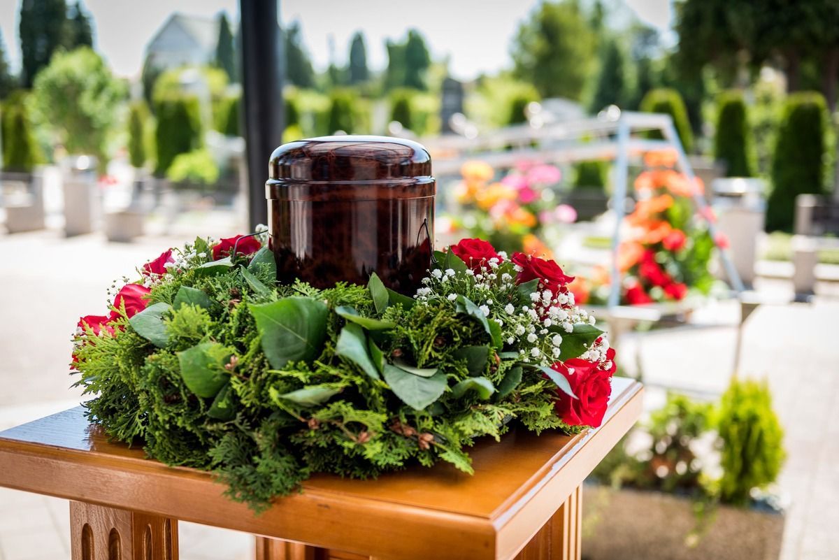 Floral wreath around a dark urn on a wooden table at an outdoor memorial garden