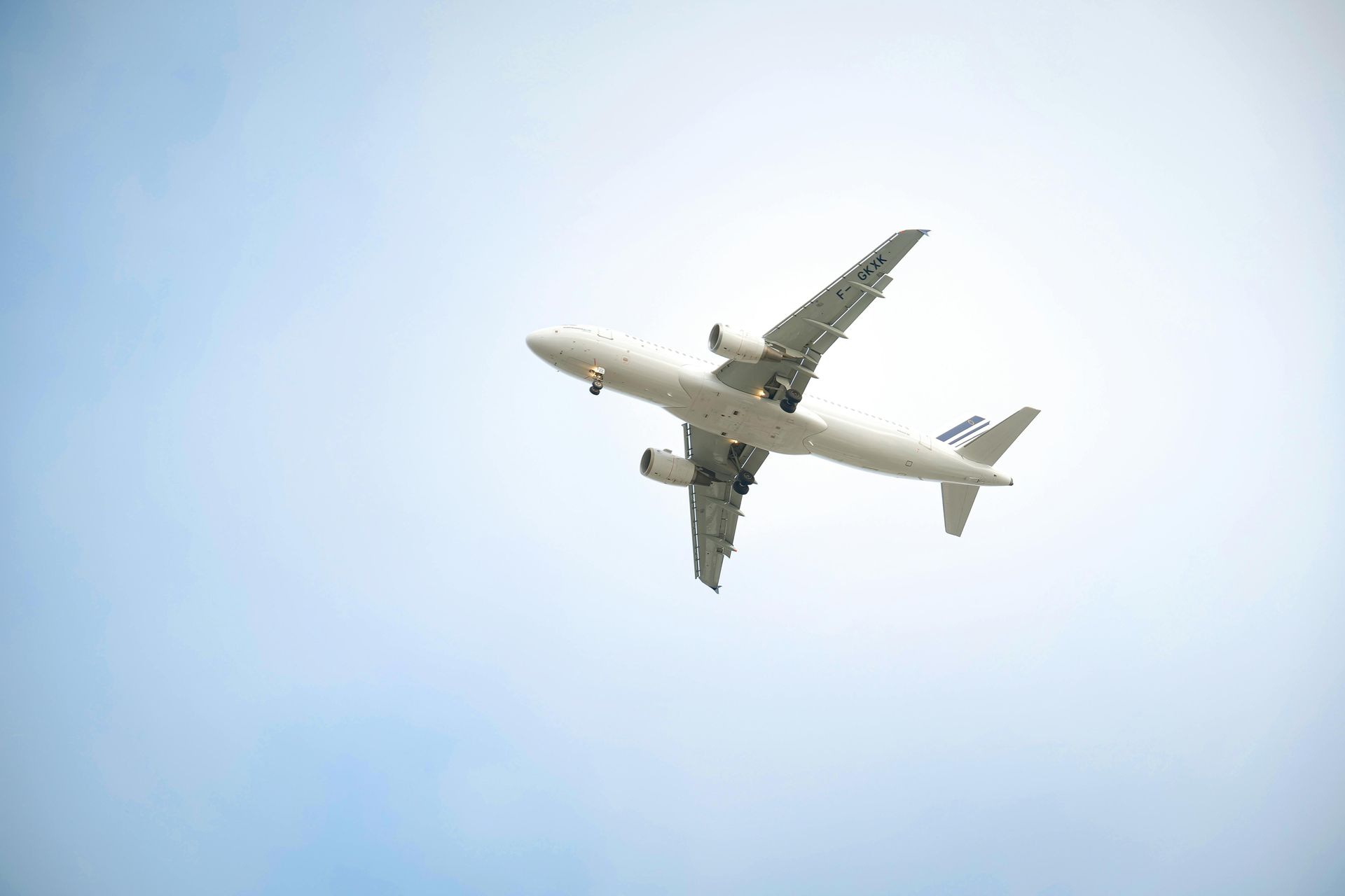 Airplane flying overhead against a pale blue sky