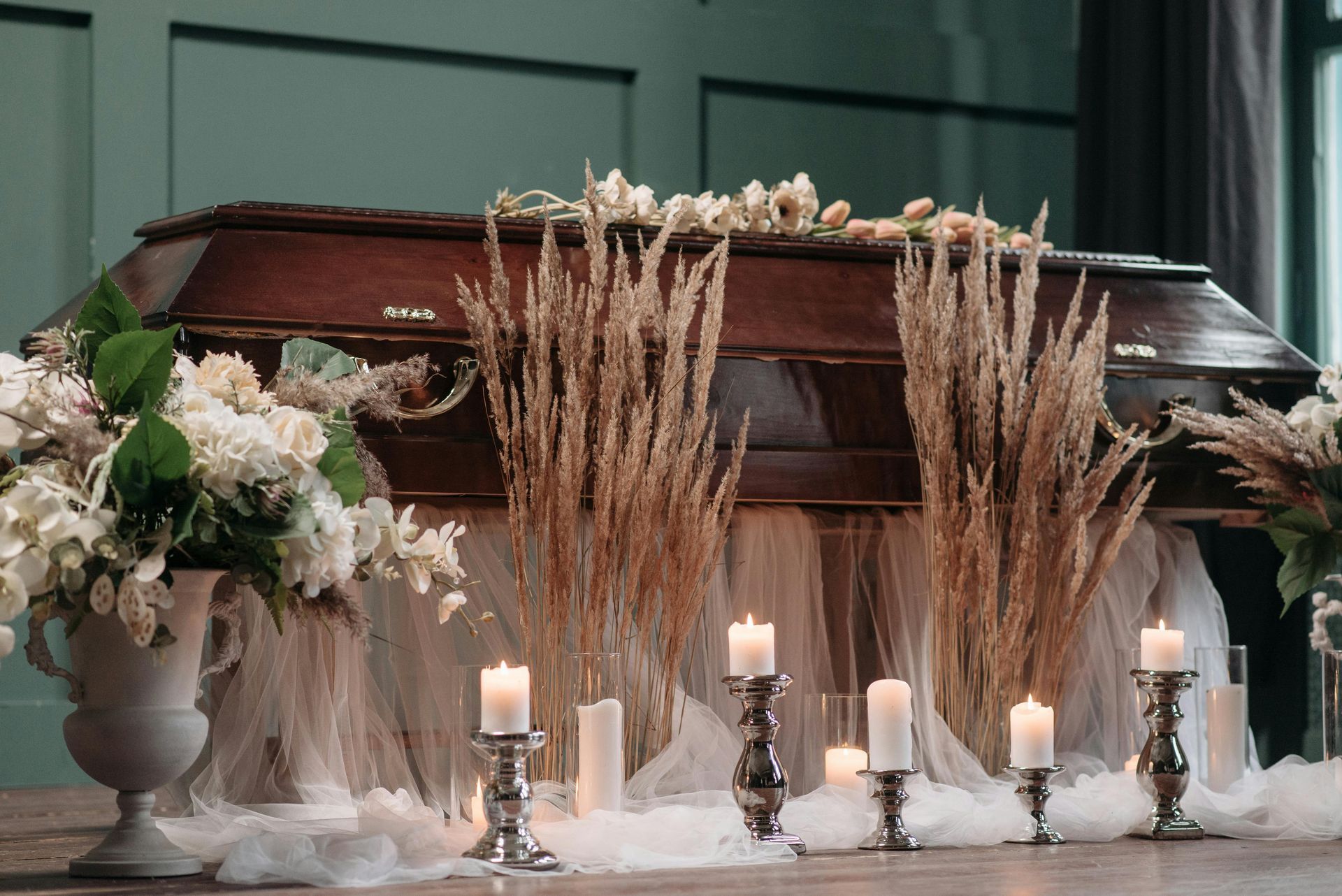 White floral funeral casket display with candles and dried wheat on a dark green backdrop