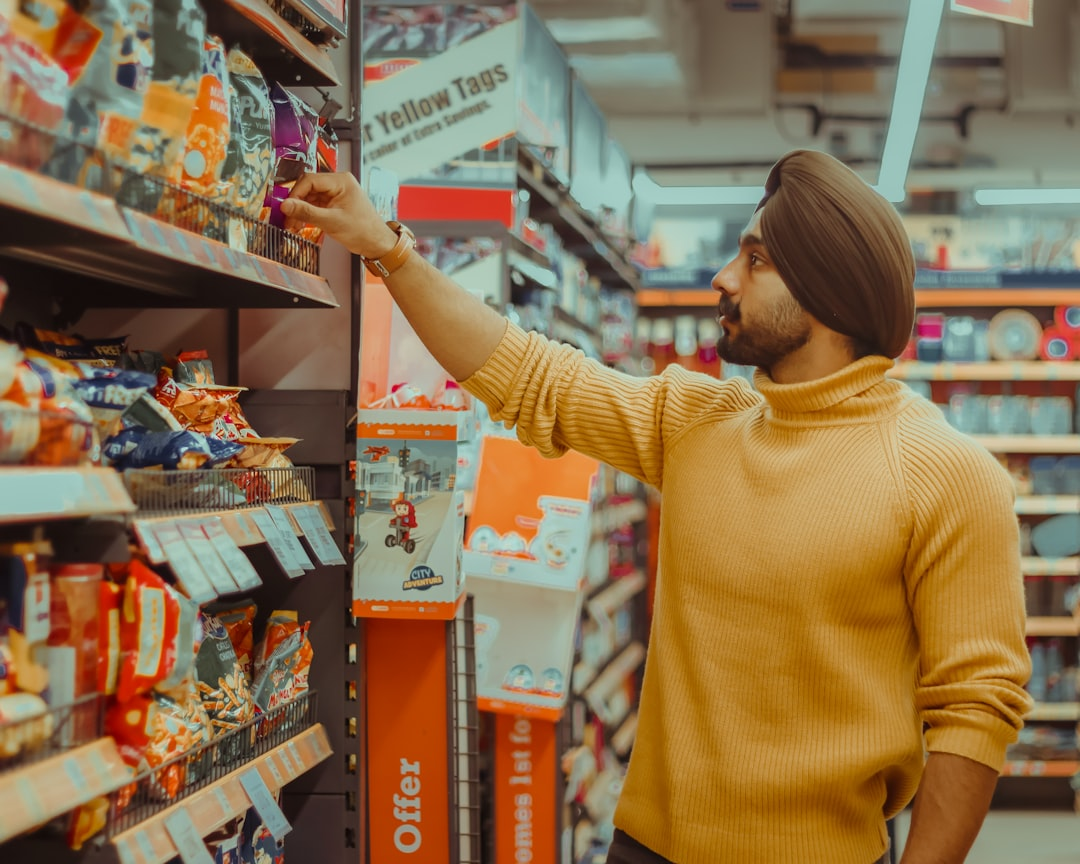 A man in a yellow sweater and turban reaches for a snack on a supermarket shelf.