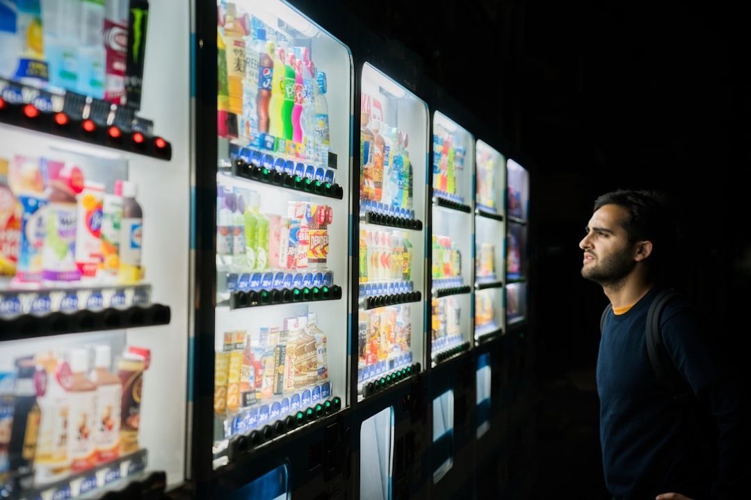 Man looking at a row of lit vending machines filled with snacks and drinks in a dark setting.