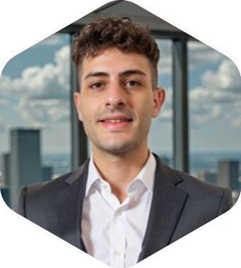 Young man in a suit and white shirt, smiling at the camera, in front of a city skyline.