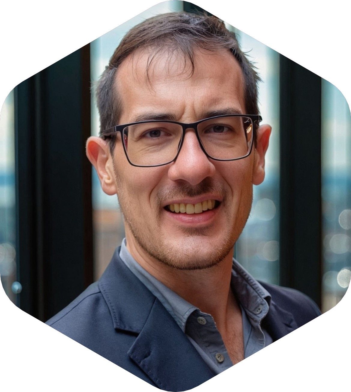 Smiling man in glasses and blazer, set against a blurred urban backdrop.