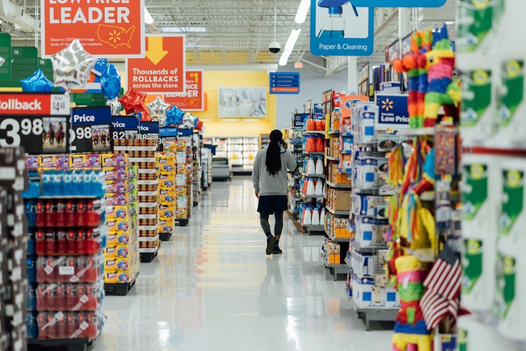 Person walking down an aisle in a Walmart store, surrounded by shelves of merchandise. Bright overhead lights illuminate the space.