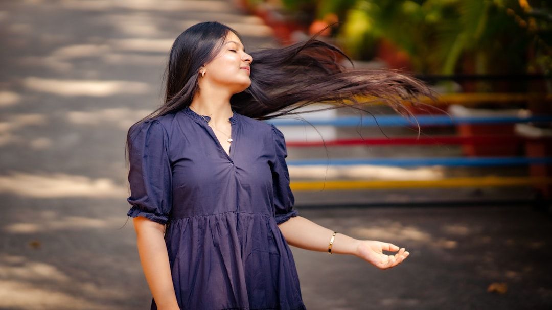 Woman with long black hair tossing it back, wearing a navy dress in a park.