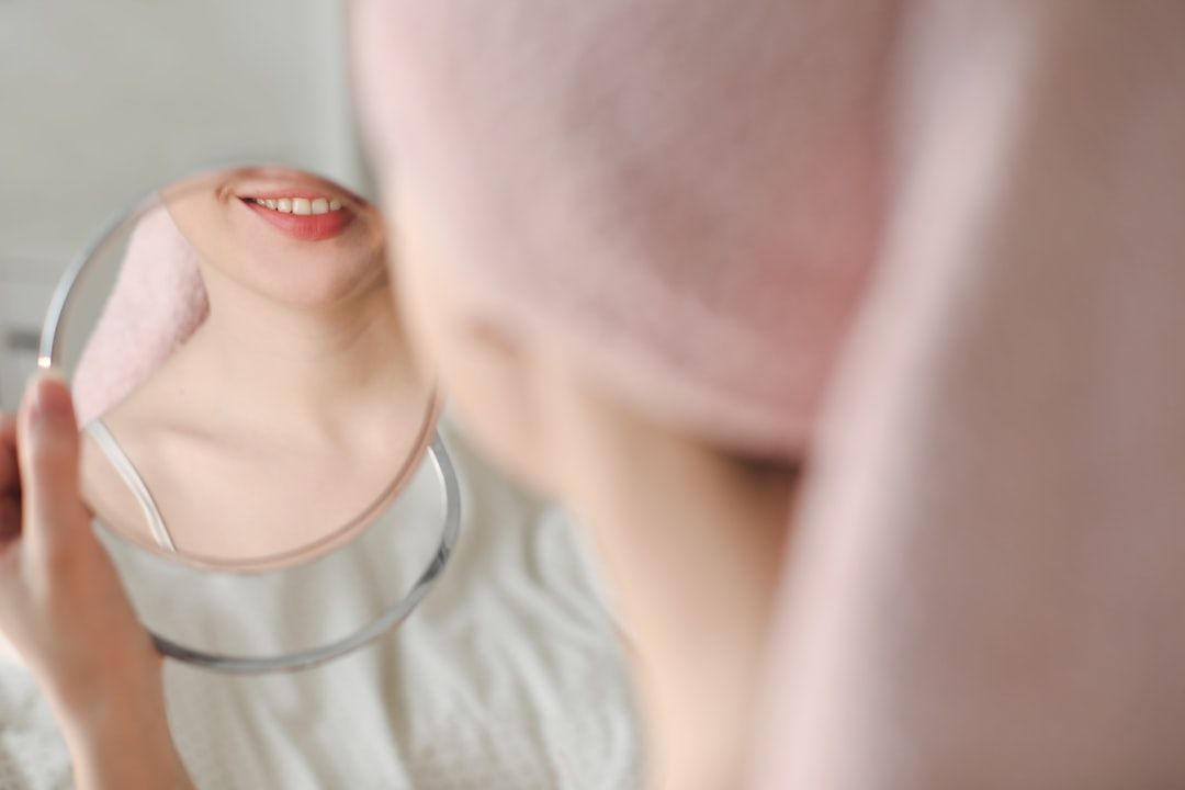 Person holding a mirror, smiling while looking at their reflection. The person is wearing a pink towel and light-colored top.