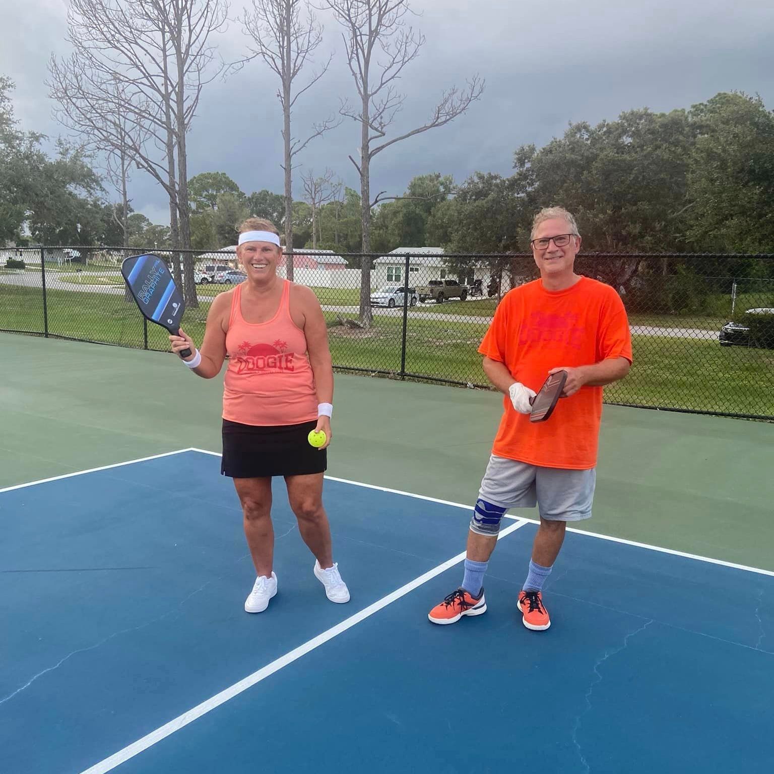 A man and a woman are standing on a tennis court holding tennis rackets.