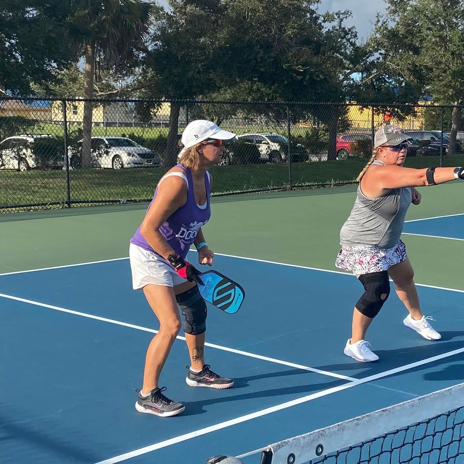 Two women are playing a game of pickleball on a tennis court