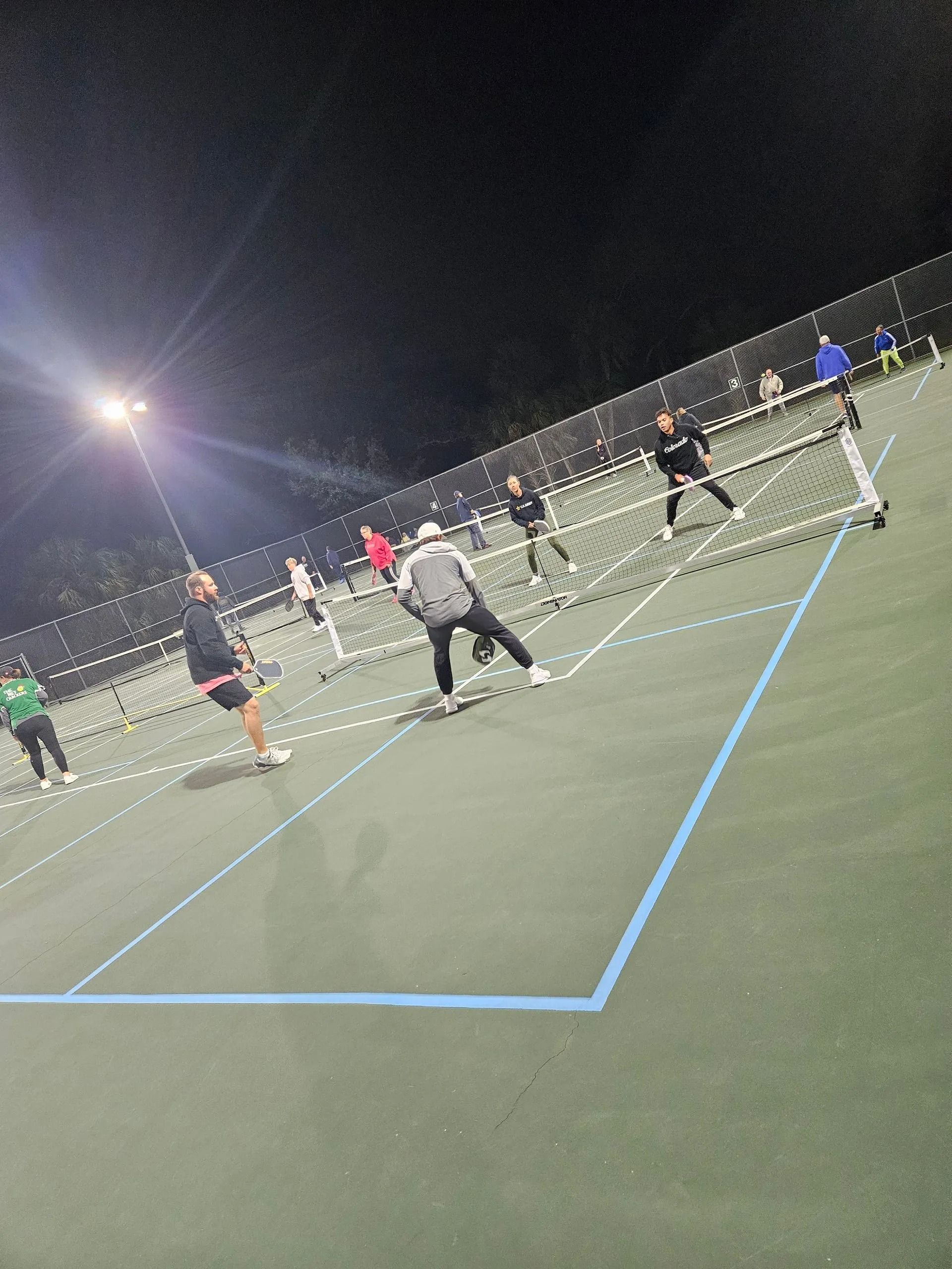 A group of people are playing tennis on a tennis court at night.