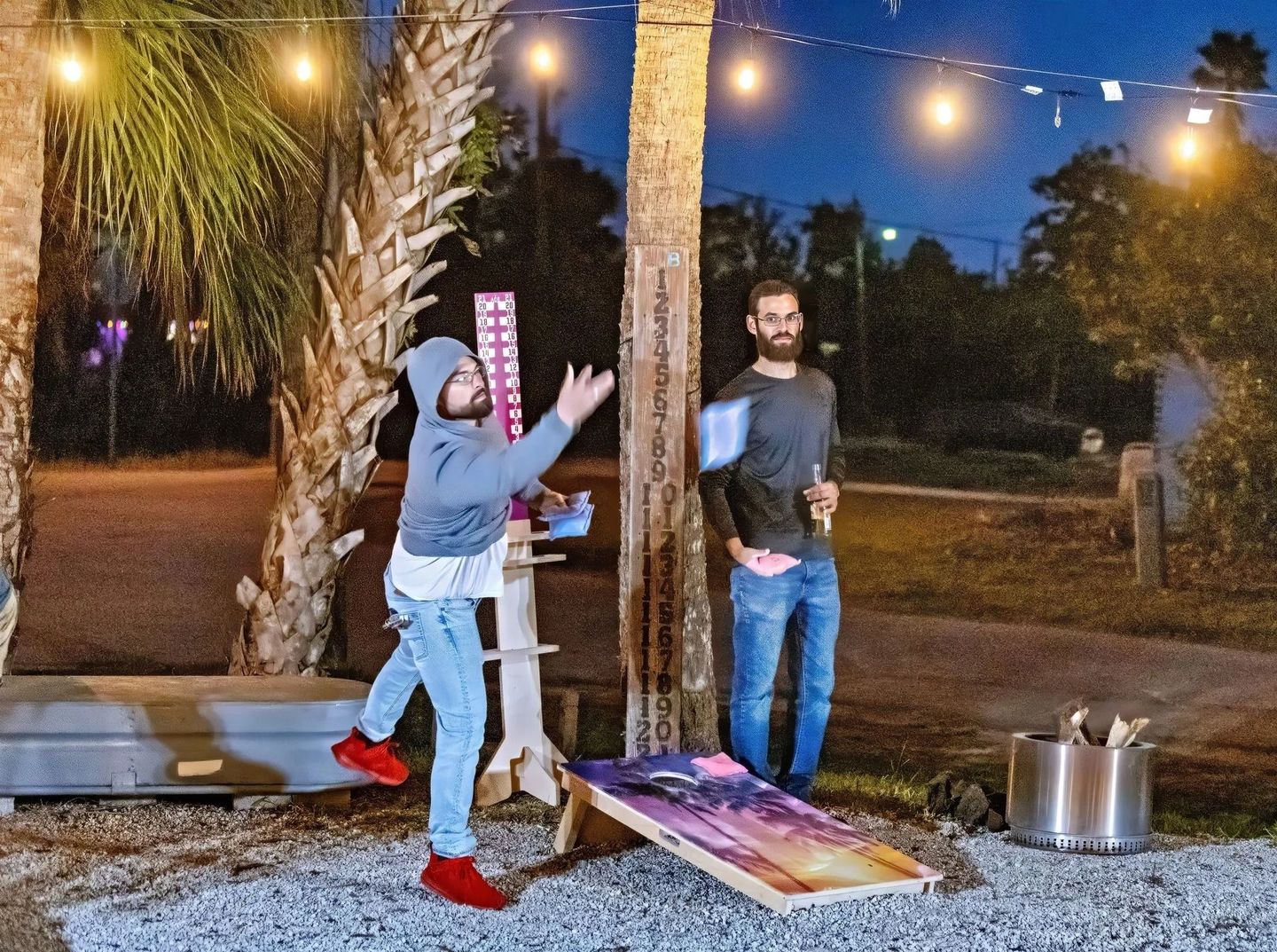 Two men are playing a game of cornhole outside at night.