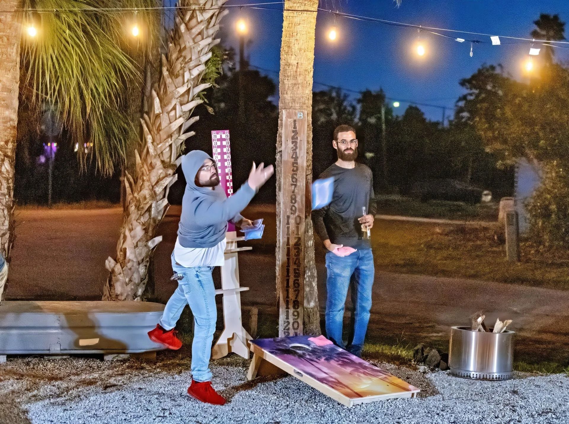 Two men are playing a game of cornhole outside at night.