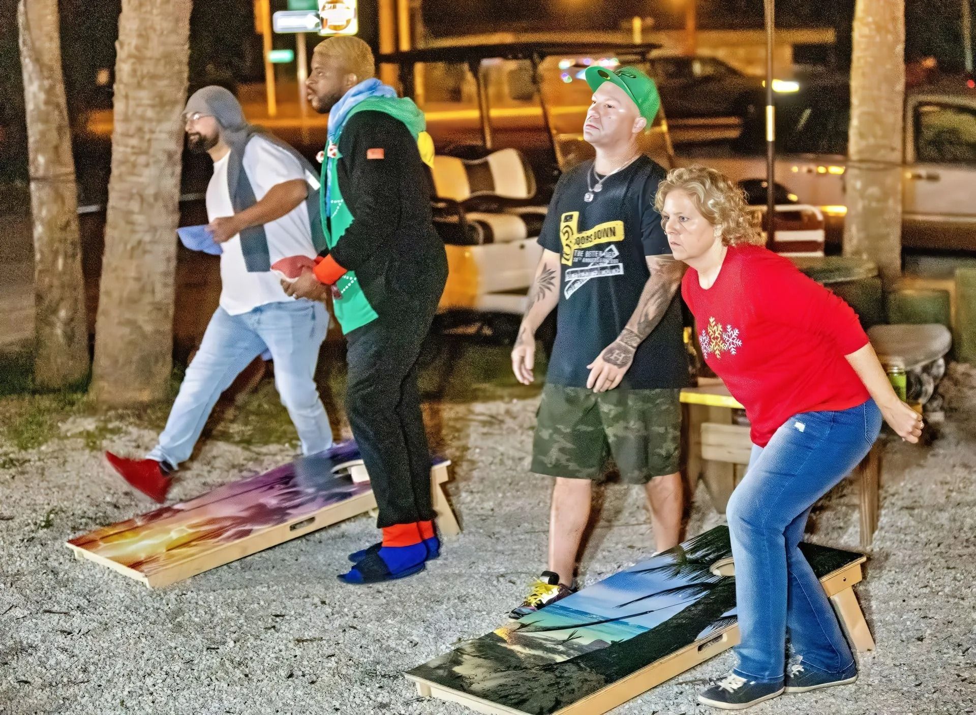 A group of people are playing a game of cornhole outside at night.