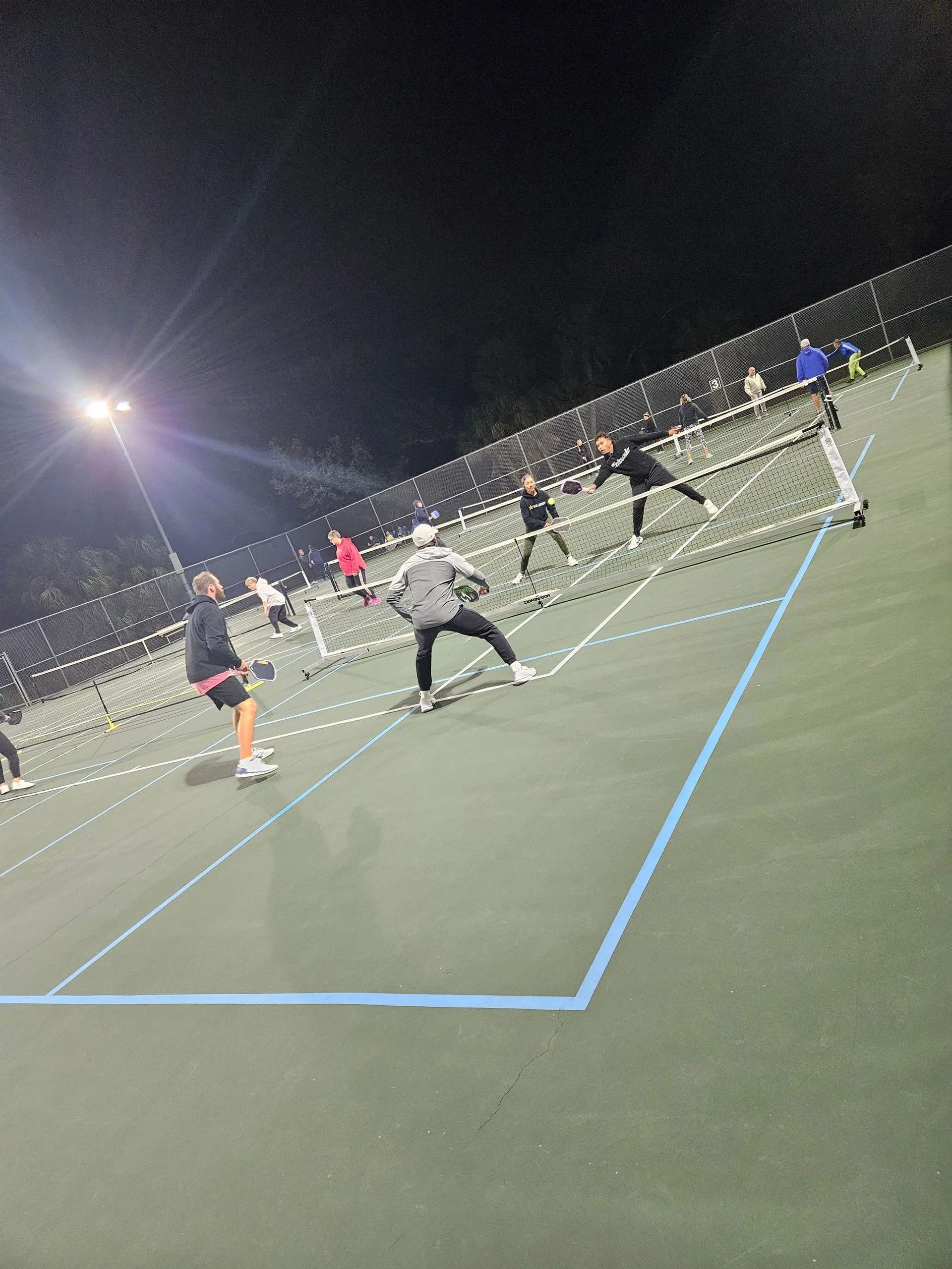 A group of people are playing tennis on a court at night.
