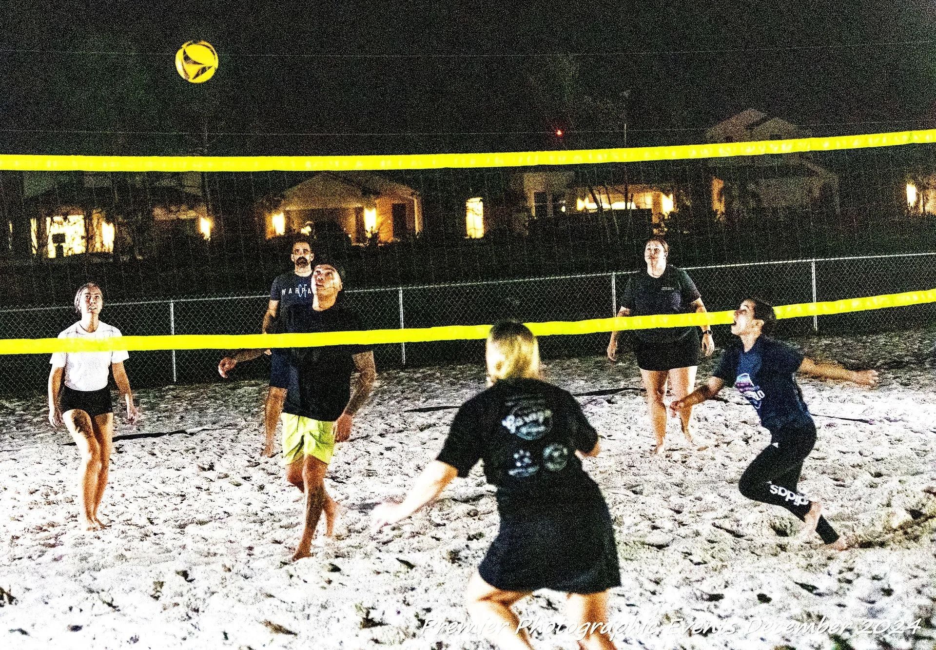A group of people are playing volleyball on a beach at night