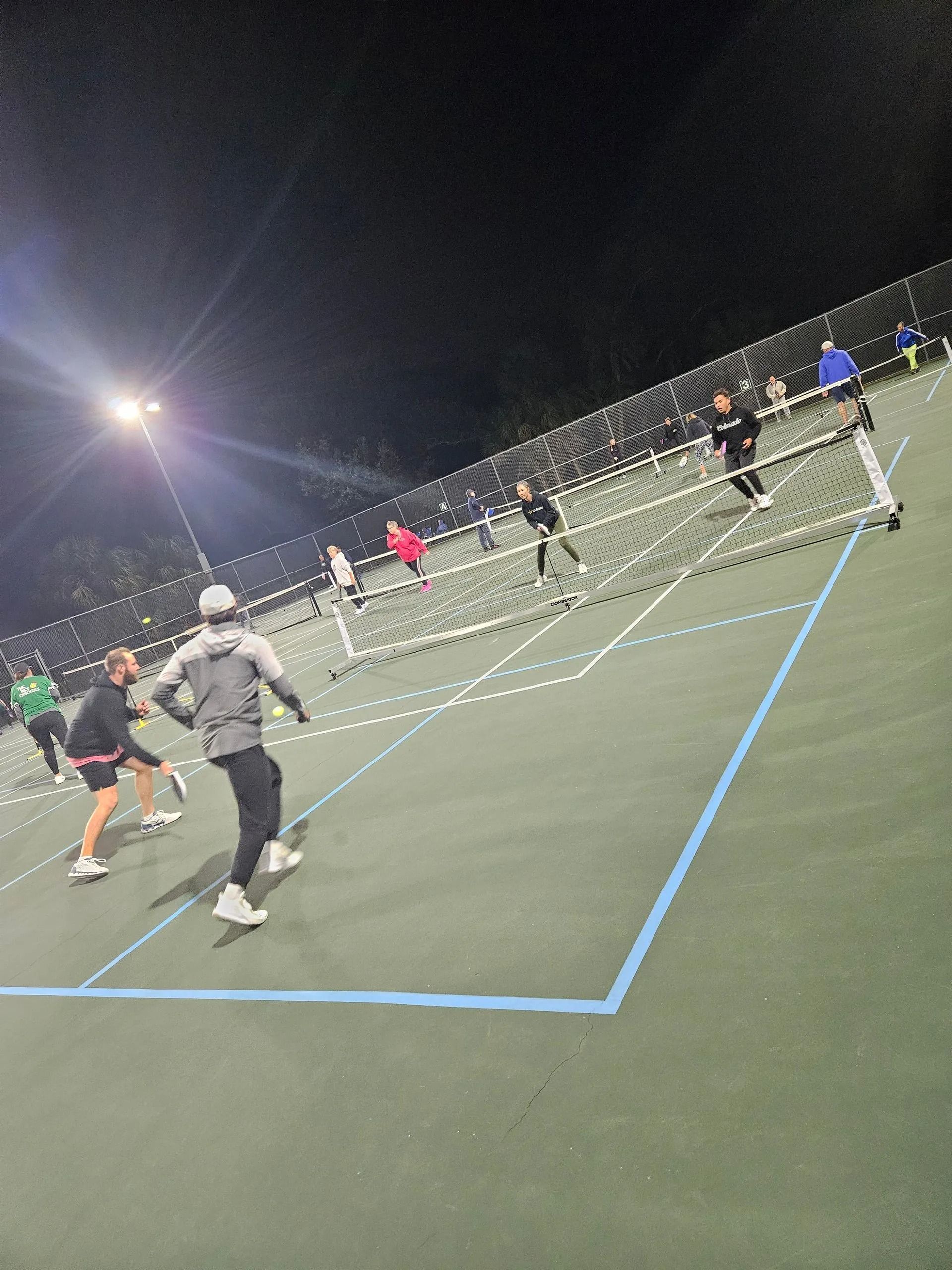 A group of people are playing tennis on a court at night.