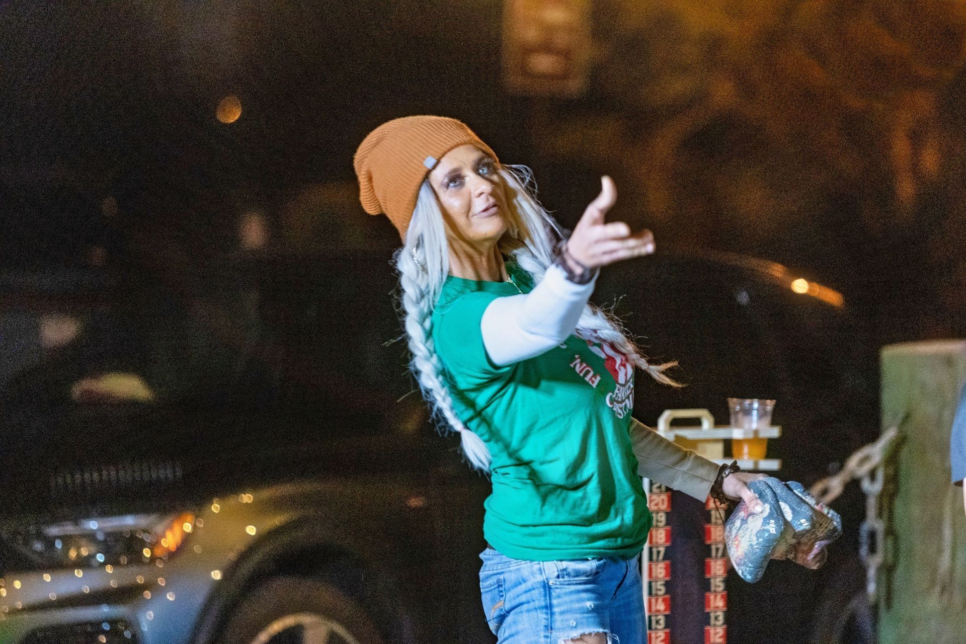 A woman wearing a green shirt and a beanie is standing in front of a car.