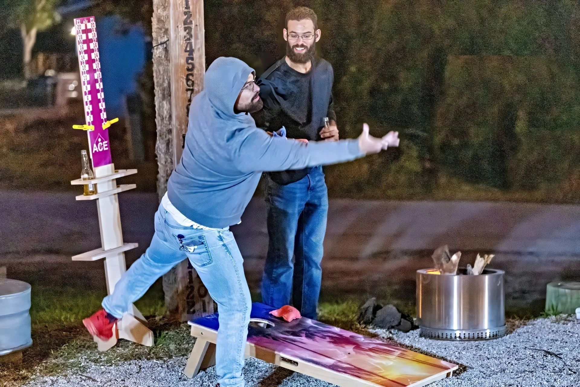 Two men are playing a game of cornhole outside at night.