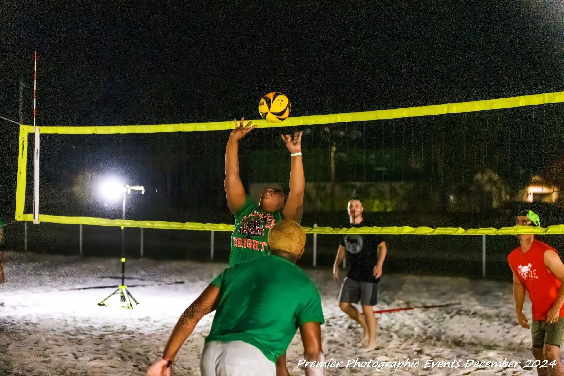 A group of people are playing volleyball on a beach at night.