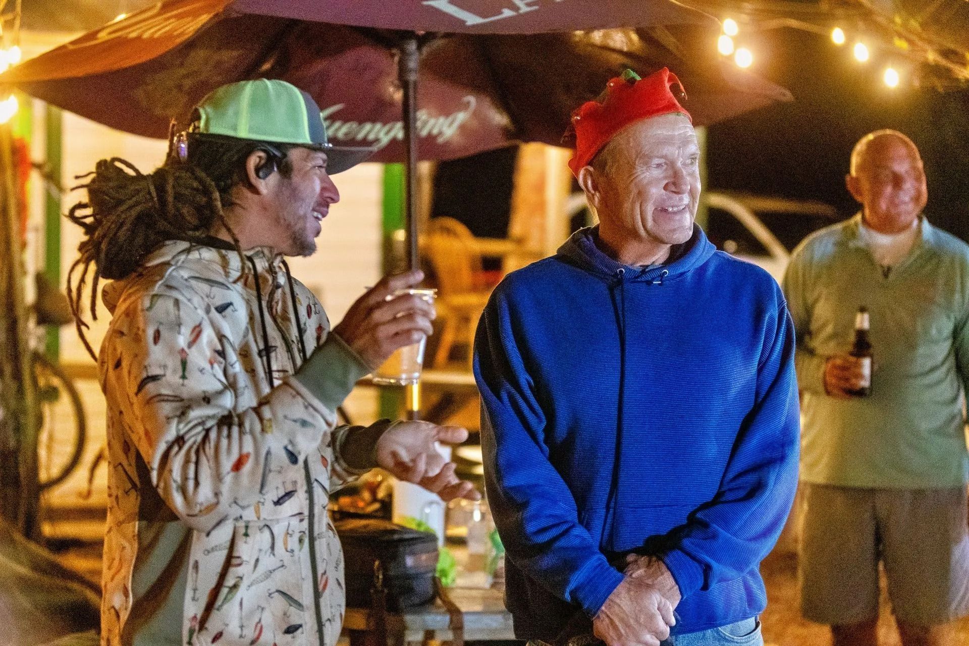 Two men are standing under an umbrella talking to each other.