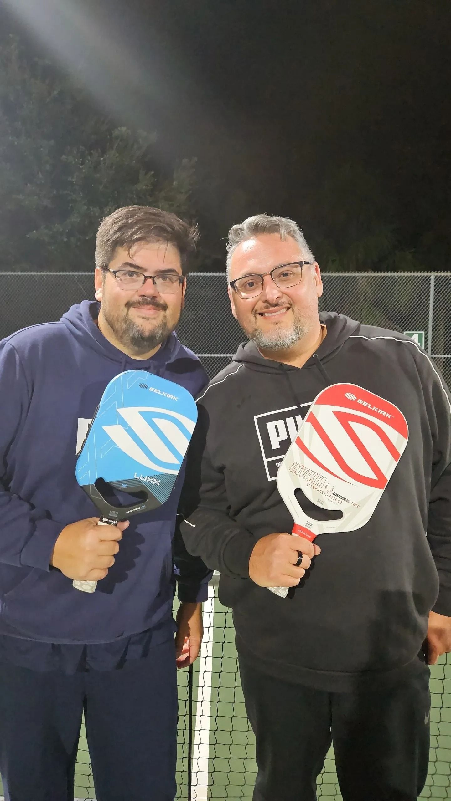 Two men are standing next to each other on a tennis court holding paddle rackets.
