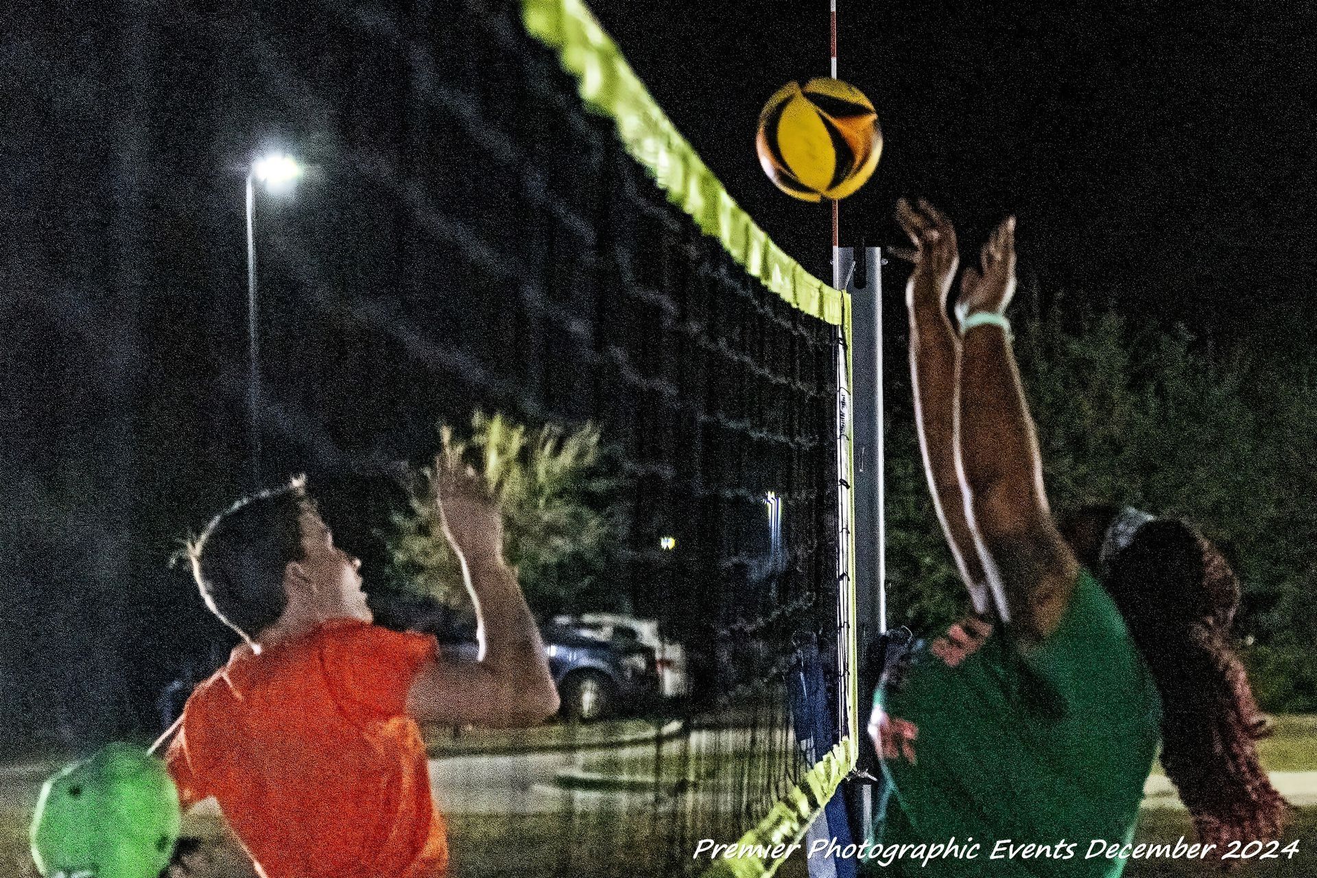 Two people are playing volleyball on a court at night.