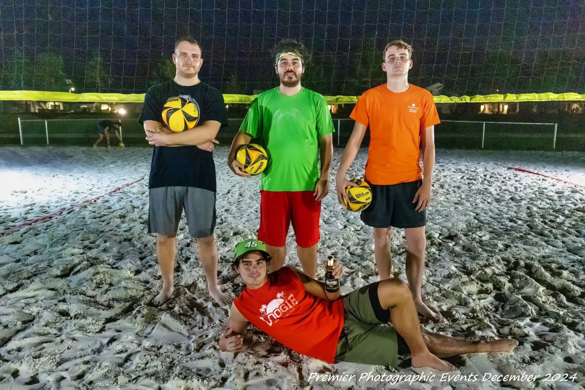A group of men are standing on a sandy beach holding volleyballs.