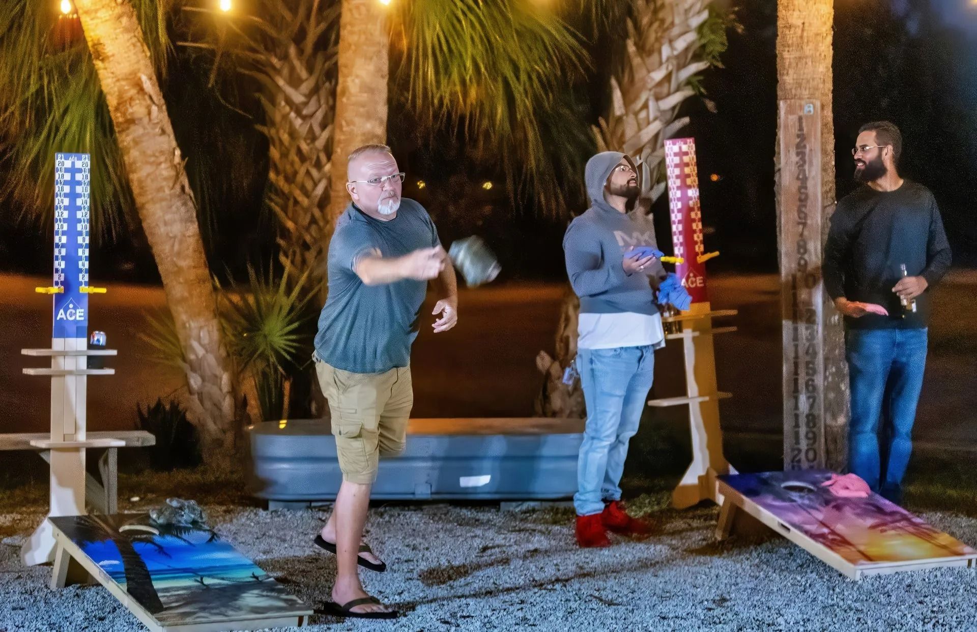 Three men are playing a game of cornhole outside at night.