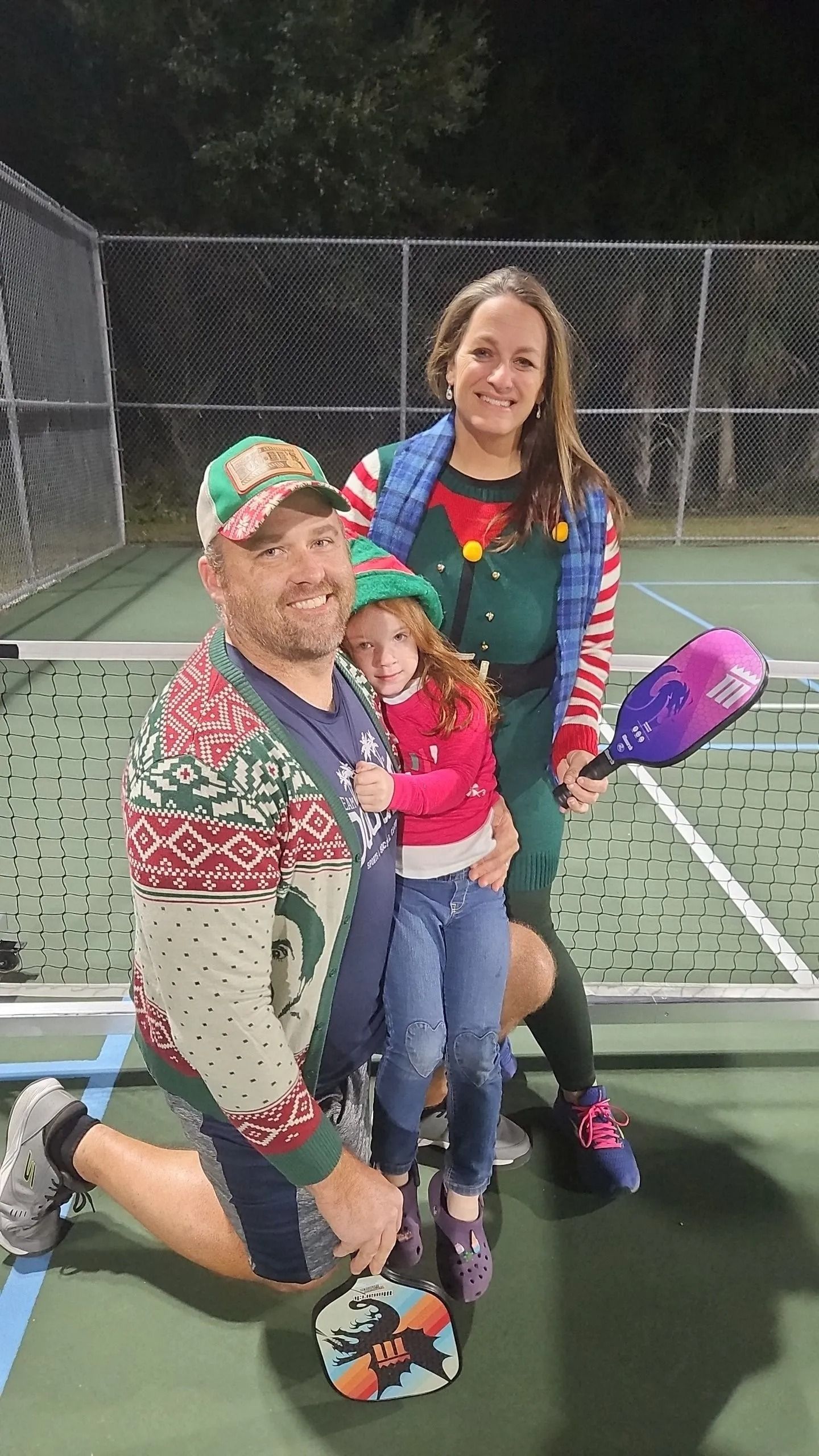 A man , woman and child are posing for a picture on a tennis court.