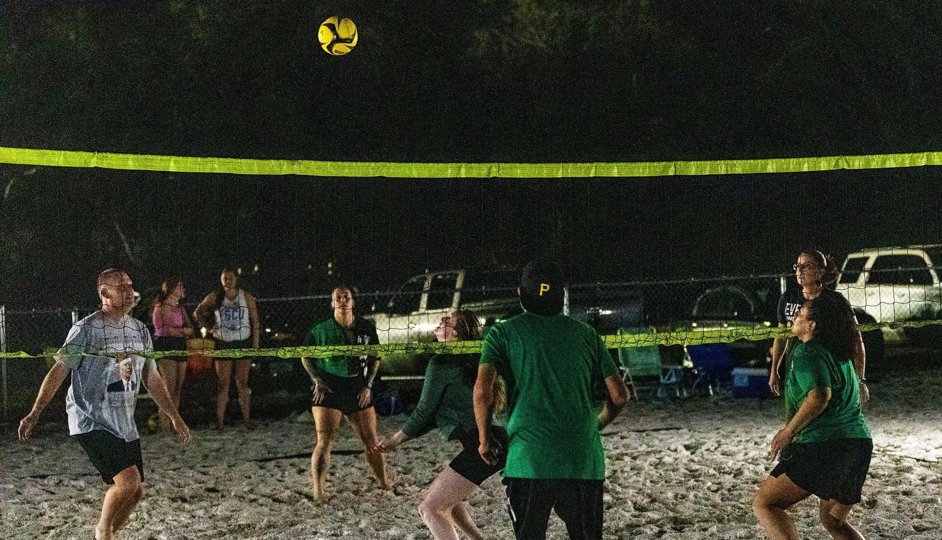 A group of people are playing volleyball on a beach at night.