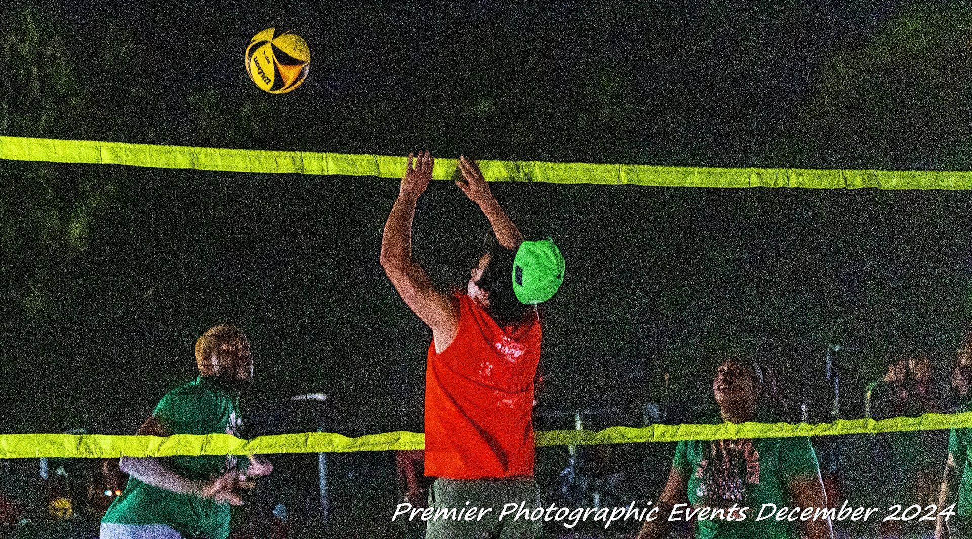 A man in a red shirt is jumping to catch a volleyball.