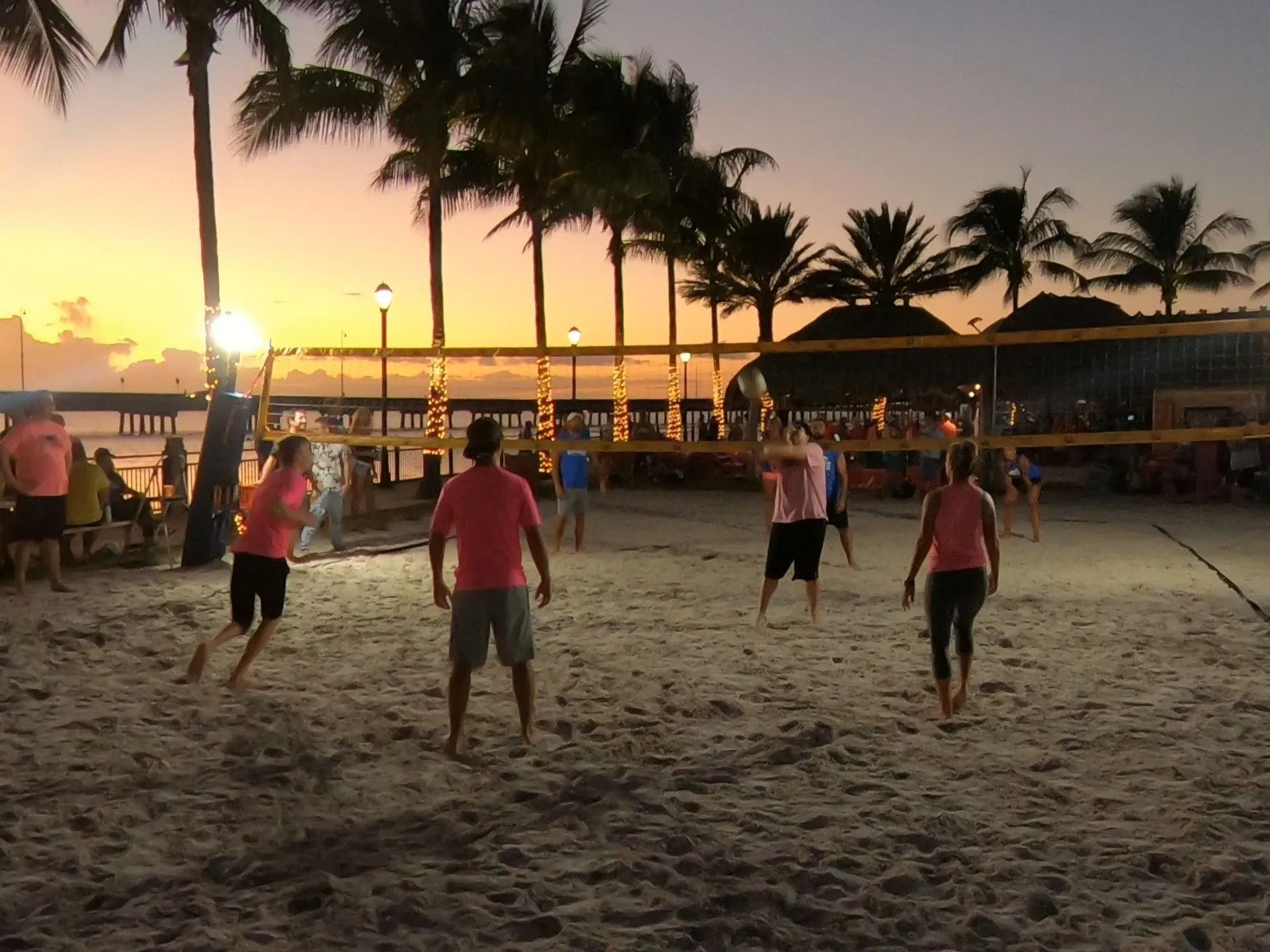 A group of people are playing volleyball on a beach at sunset