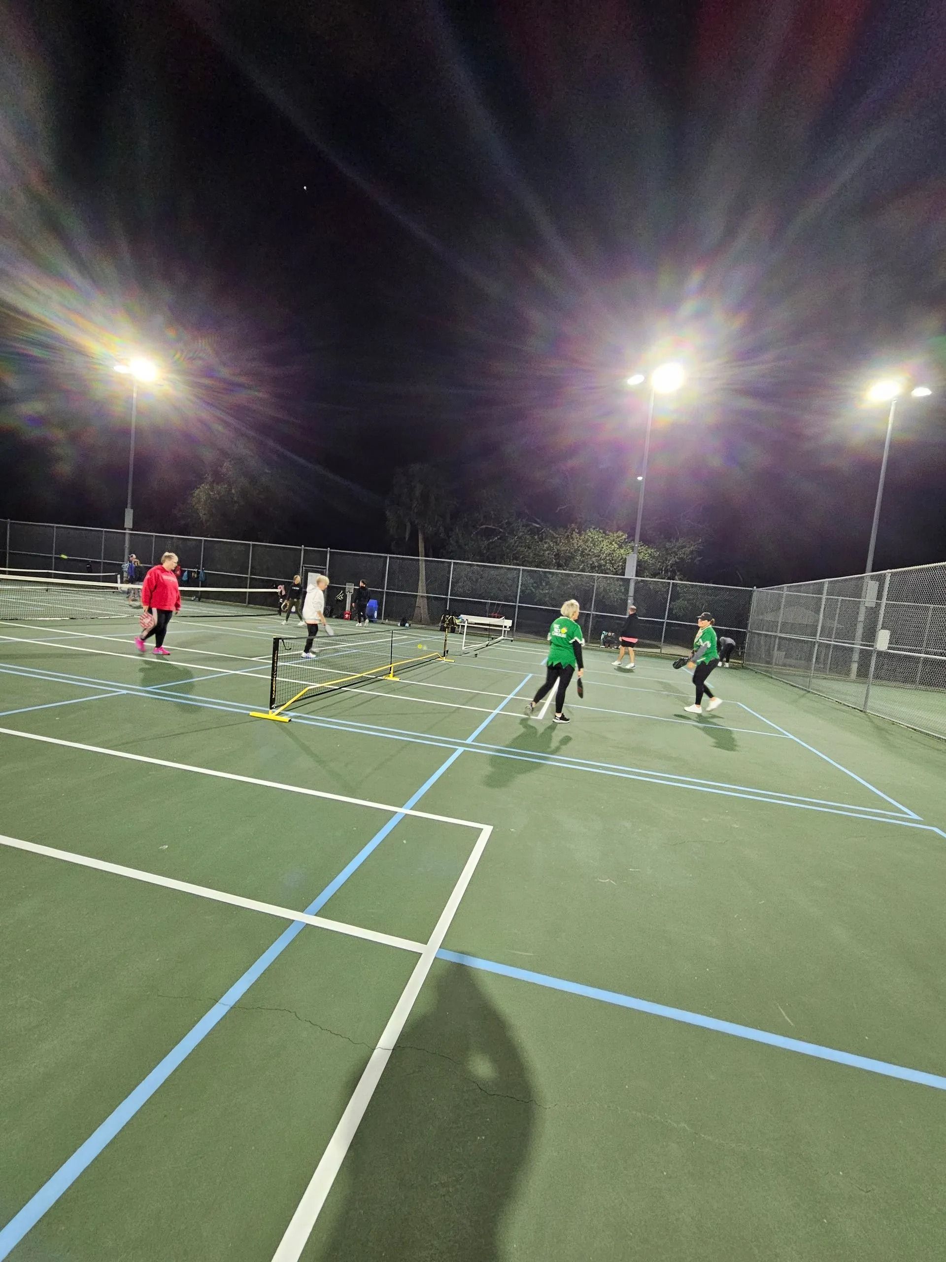 A group of people are running on a tennis court at night.